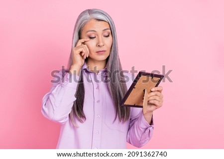 Portrait of attractive sad sullen gray-haired woman looking at photo crying isolated over pink pastel color background