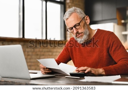 Mature middle-aged businessman freelancer man counting domestic bills on calculator at home using laptop. Debt loan e-banking. Mortgage concept Royalty-Free Stock Photo #2091363583