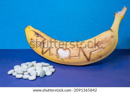 a ripe banana with a cardiogram cut out on the peel and a heart next to a mountain of pills. background picture.