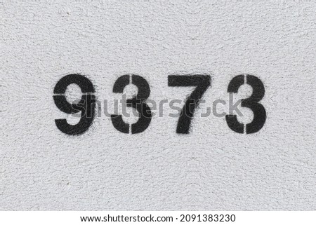 Black Number 9373 on the white wall. Spray paint. Number nine thousand three hundred and seventy three.