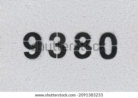 Black Number 9380 on the white wall. Spray paint. Number nine thousand three hundred and eighty.