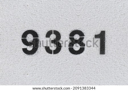 Black Number 9381 on the white wall. Spray paint. Number nine thousand three hundred and eighty one.