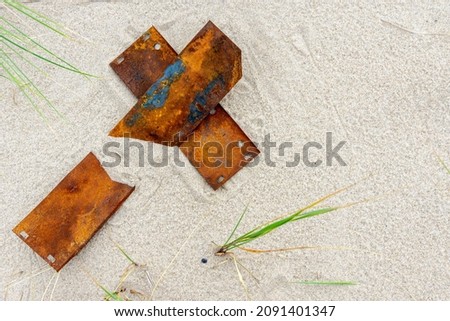 The letter "X" on the sand is made of rusty plates. Metal plates lie on the sandy shore. A letter from the alphabet. Place for the inscription. An unusual letter.