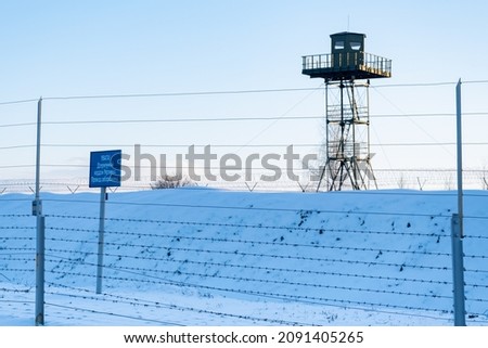 Surveillance tower, iron fence and caution banner with an inscription in Belarusian "Attention! State border of Ukraine. No entry". Closed area. Border protection and illegal migration concept