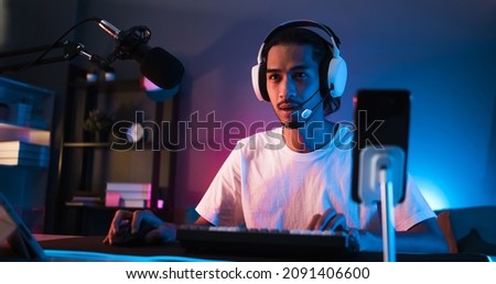 Young confident Asian man playing online computer video game, colorful lighting broadcast streaming live at home. Gamer lifestyle, E-Sport online gaming technology concept Royalty-Free Stock Photo #2091406600