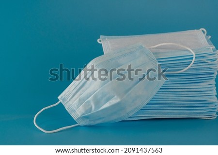 There are many new medical surgical three-layer masks stacked high and one used mask lies next to it on a blue background