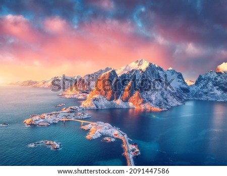 Beautiful landscape with blue sea, snowy mountains, rocks and islands, village, rorbu, road, bridge and pink sky at sunrise. Aerial view. Hamnoy in snow in winter in Lofoten islands, Norway. Top view Royalty-Free Stock Photo #2091447586