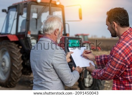 Farm worker signing a contract with sales representative at cultivated land.