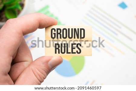 Cropped view of hands holding wooden cube with GROUND RULES lettering on work table. Top view