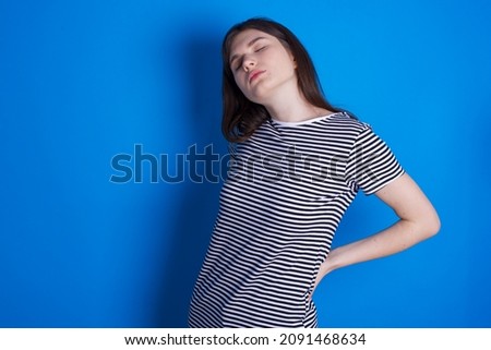 Caucasian woman wearing striped T-shirt isolated over blue background got back pain