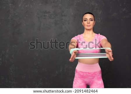 Fitness sportive woman over black background. Photo of an attractive woman in fashionable sportswear. Stretches the elastic band, looks at the camera. Sports and healthy lifestyle