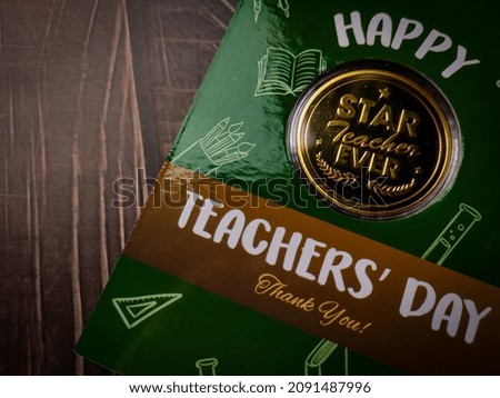 Green card and coins written with text Happy Teachers day on wooden background.