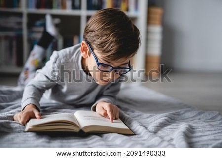 One caucasian boy lying on the floor at home in day reading a book front view copy space real people education concept Royalty-Free Stock Photo #2091490333