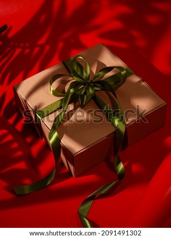 gift box with green ribbon and red background with shadow, selective focus, blurry.