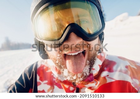 Portrait smile young bearded man with fresh snow holding snowboard background of ski resort lift, sun light.