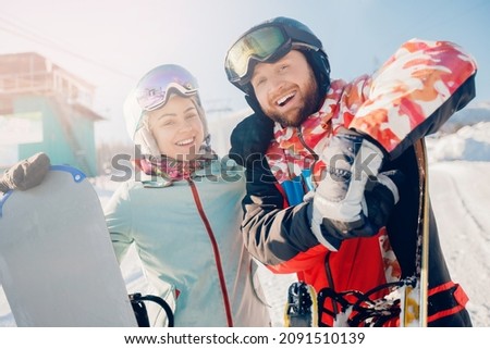 Happy young lover couple man and woman snowboarders on background of ski resort, sun light.