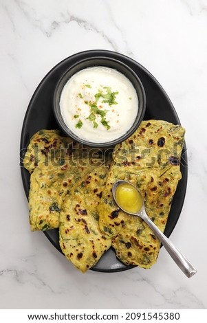 A Food called Methi paratha or Methi thepla is an Indian breakfast dish served with curd and a spoon full of desi ghee. with copy space. Indian fenugreek flatbread. Healthy lunch or dinner. Royalty-Free Stock Photo #2091545380