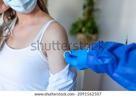 Female doctor in protective face mask and gloves preparing to inject pregnant patient with covid antiviral vaccine, rubbing hand with cotton pad. Mass vaccination centre, global immunization campaign