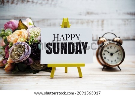 Happy Sunday text with flower bouquet and alarm clock on wooden background