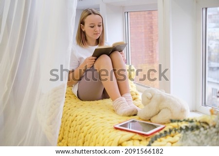 teenage girl sits on the windowsill by the window and draws or writes in the diary. cute girl watching video on tablet