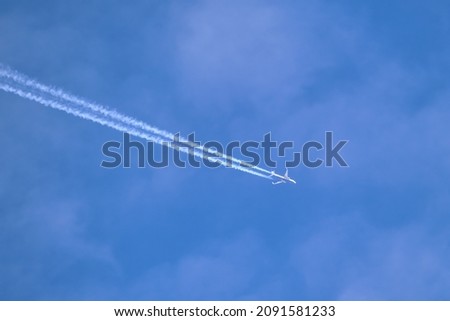 Distant passenger jet plane flying on high altitude through white clouds on blue sky leaving white smoke trace of contrail behind. Air transportation concept Royalty-Free Stock Photo #2091581233