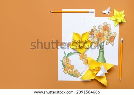 Origami narcissus flowers and greeting cards on color background