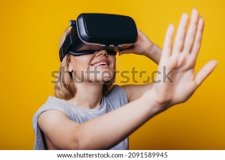 Close-up portrait of a caucasian woman touching air during the VR experience isolated on yellow background.