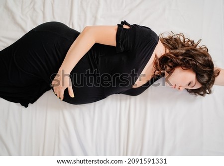 attractive pregnant woman in black dress in bed. beauty, tenderness of motherhood. vitamins, cosmetics for pregnant women. medical examinations and tests. sale of clothes for expectant mothers