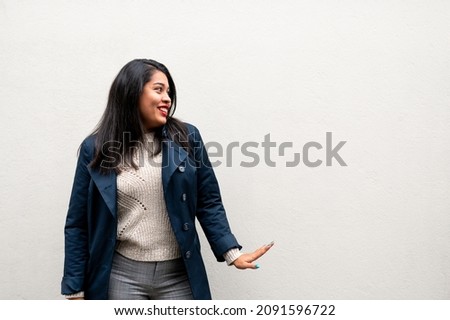 Young latin woman with smiling face gesturing looking at her side. Isolated white background with copy space.