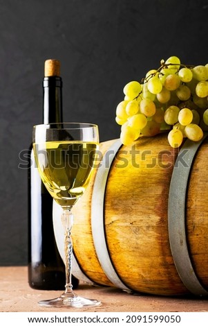a bottle of wine a glass an oak barrel and a bunch of white grapes on a dark background. High quality photo