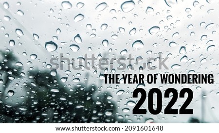 A quote - "2022 THE YEAR OF WONDERING", with drops of water on the window. A new year celebration concept photo. A copy space for text or words.