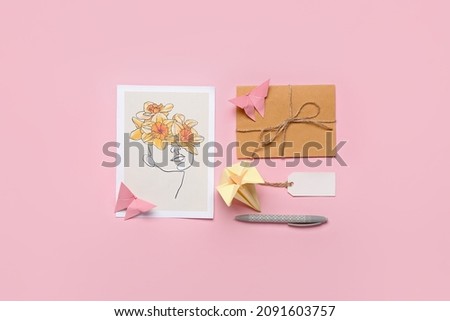 Origami narcissus flower, pen and greeting card on color background