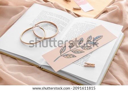 Book with bookmark and earrings on color background