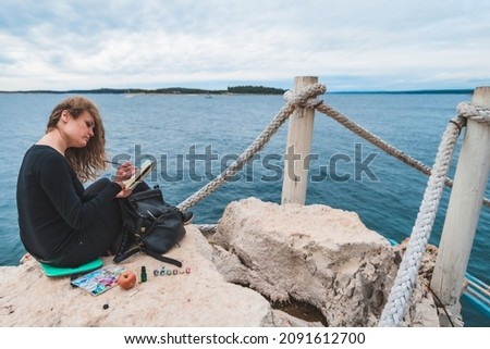 woman sitting at the edge drawing picture of seascape suspension bridge