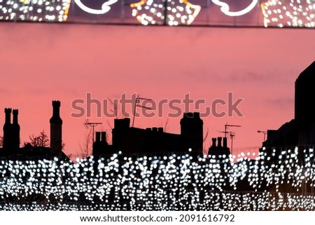 Christmas shopping town centre lights with chimneys and shops silhouetted at sunset. Beautiful pink winter sky with tv aerials and street illuminations ready for xmas.