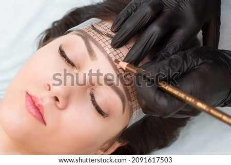 Permanent eyebrow makeup. The master draws a sketch before the permanent makeup procedure with a brown pencil and a ruler.