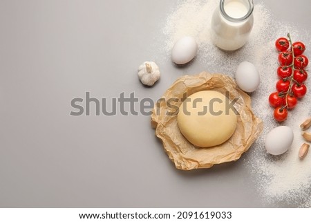 Parchment with dough and ingredients for preparing pizza on grey background