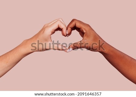 Close up of black and white female hands in heart shape, interracial friendship. Multiracial hands over beige background at studio. Peace and love concept. Royalty-Free Stock Photo #2091646357