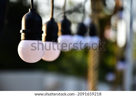 White bulbs which hanging on wire to decorate the area around the house during christmas day at night, blurred background, soft and selective focus on first bulb.