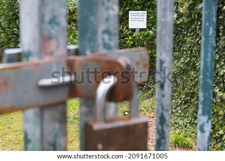 A sign that reads "No unauthorized persons. Enter at your own risk" behind a gate locked with a half-rusted padlock.