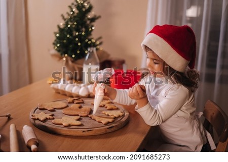 Little girl in santa hat decorates gingerbread at home. Christmas and New Year traditions concept. Christmas bakery. Happy hollidays