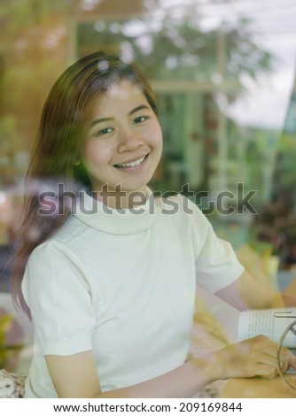 Beautiful asian woman sitting behind  the window  in cafe and reading a magazine.