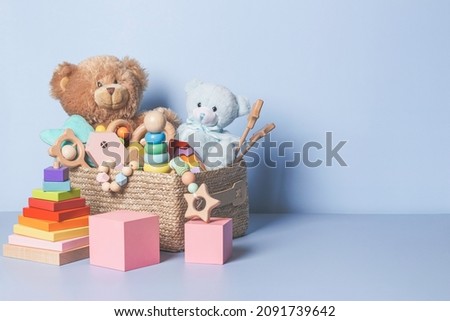 Toy box full of baby kid toys. Container with teddy bear, wooden rattles, stacking pyramid and wood blocks on light blue background. Cute toys collection for small children. Donation. Front view Royalty-Free Stock Photo #2091739642