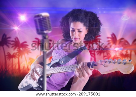 Pretty girl playing guitar against digitally generated palm tree background