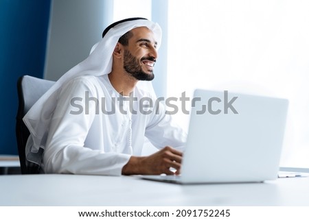 Handsome man with dish dasha working in his business office of Dubai. Portraits of a successful businessman in traditional emirates white dress. Concept about middle eastern cultures Royalty-Free Stock Photo #2091752245