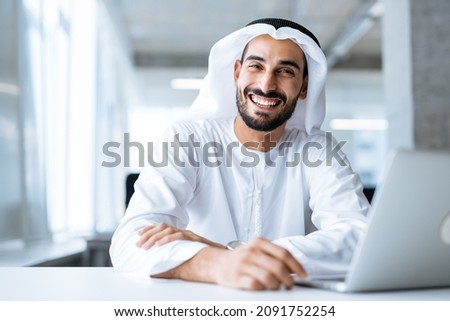 Handsome man with dish dasha working in his business office of Dubai. Portraits of a successful businessman in traditional emirates white dress. Concept about middle eastern cultures Royalty-Free Stock Photo #2091752254