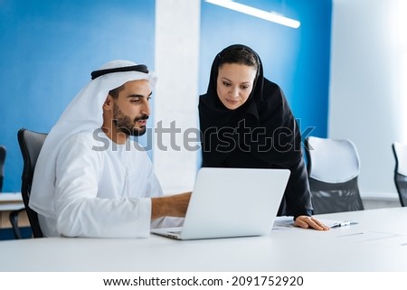 Man and woman with traditional clothes working in a business office of Dubai. Portraits of  successful entrepreneurs businessman and businesswoman in formal emirates outfits. Concept about middle east Royalty-Free Stock Photo #2091752920