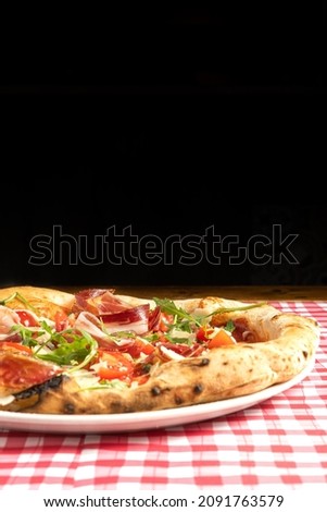 Delicious handmade pizza with italian prosciutto and iberian ham on a red and white checkered tablecloth with black background. Copy space. vertical photography. High quality photo
