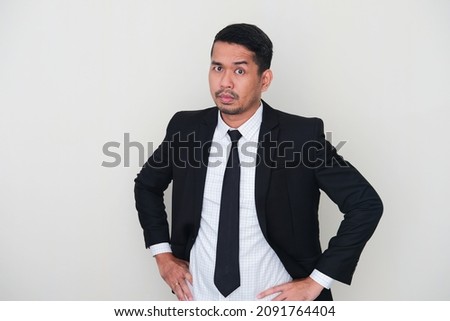 Adult Asian man wearing black suit and tie showing fierce face with his hands on hip Royalty-Free Stock Photo #2091764404