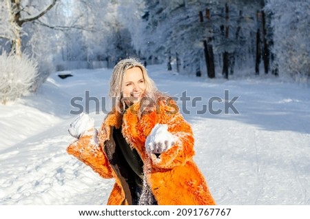 Outdoor portrait of a beautiful and happy smiling girl posing against the snow, enjoys the snow falls. Winter, Concept of Christmas, New Year, Winter Holidays and activities. Winter woman outdoors